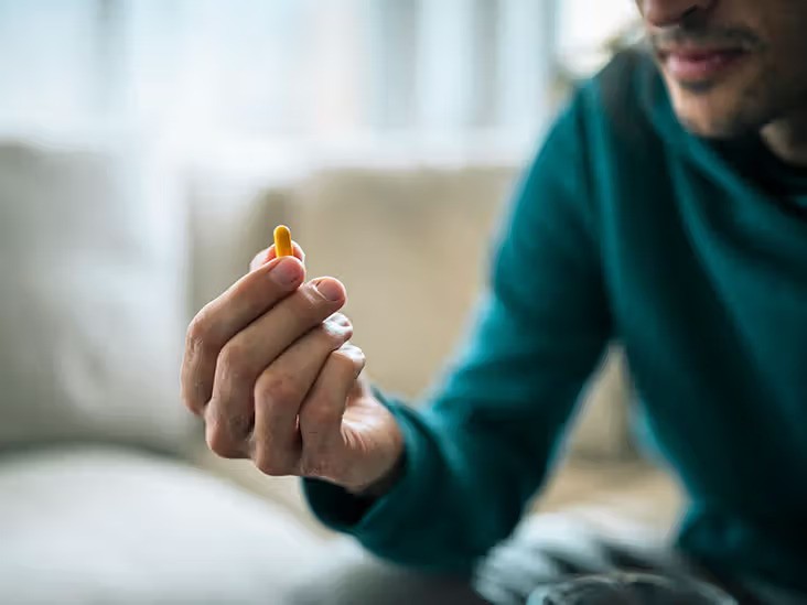 A man holds a pill in his hand, contemplating its significance and potential impact on his health.